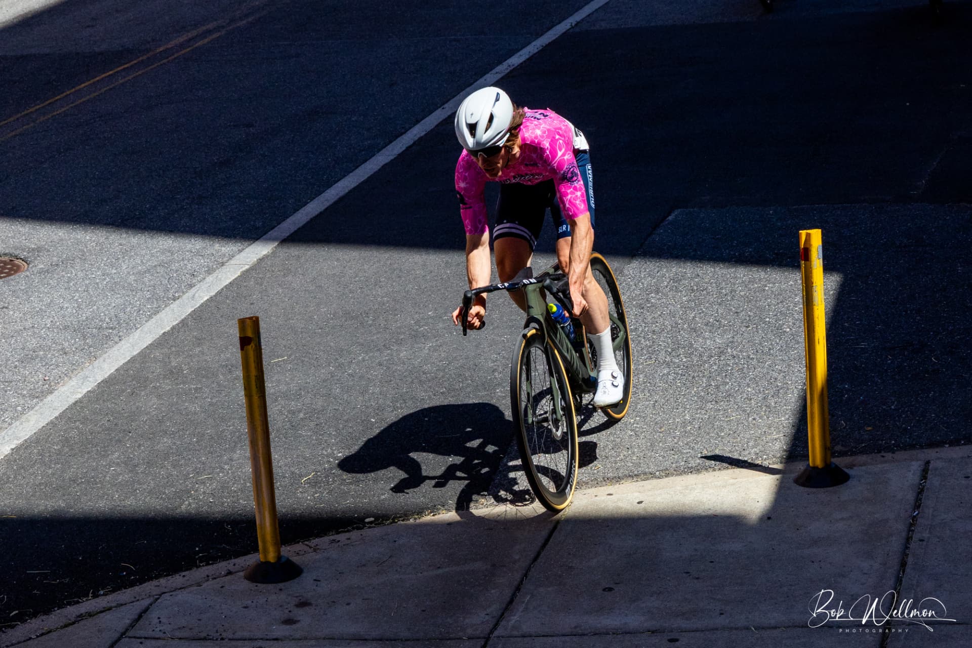 Rider in a custom pink Sportkraft jersey tucked low through a sunlit criterium corner