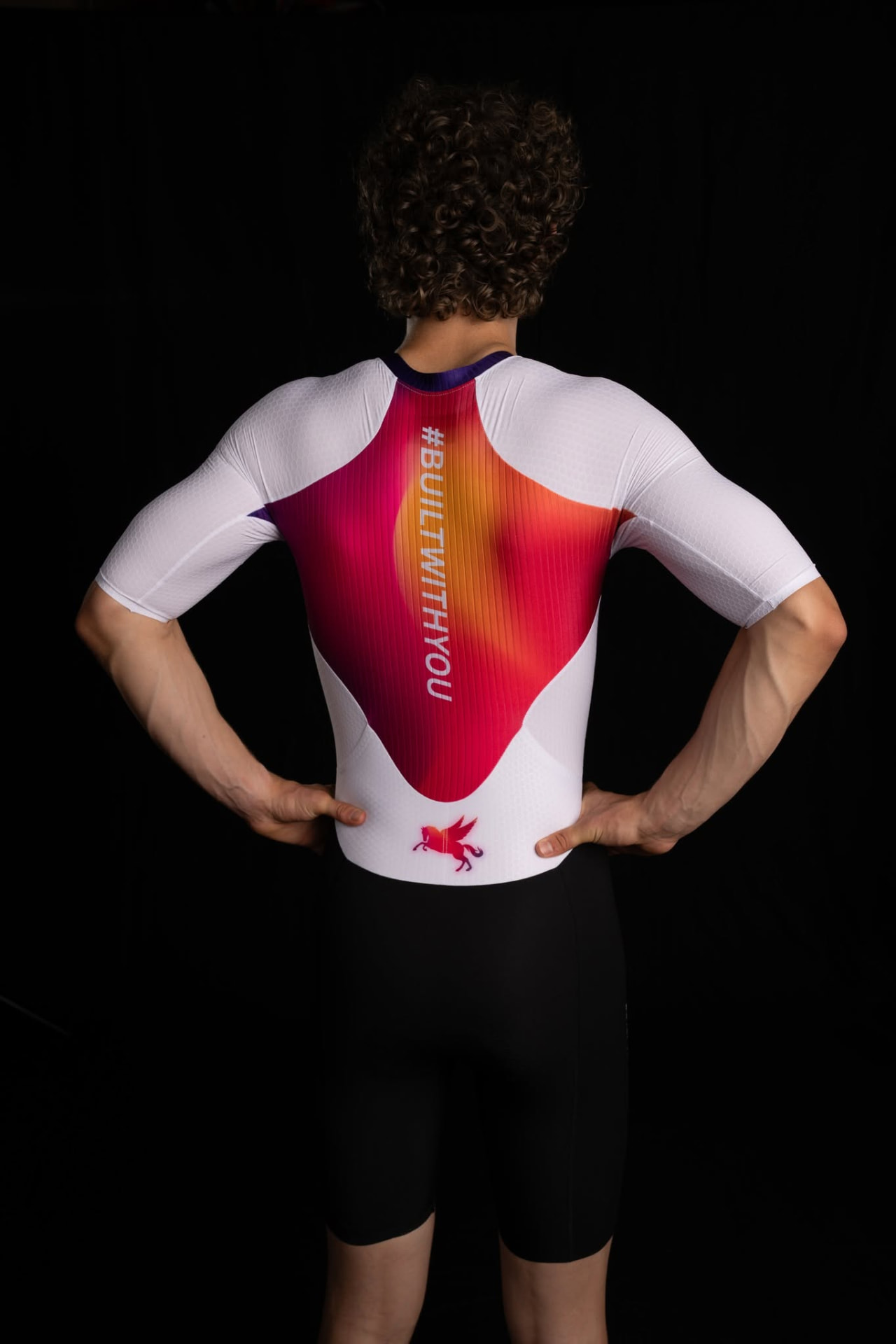 Athlete from behind in a SPORTKRAFT race suit with #BUILTWITHYOU gradient back panel