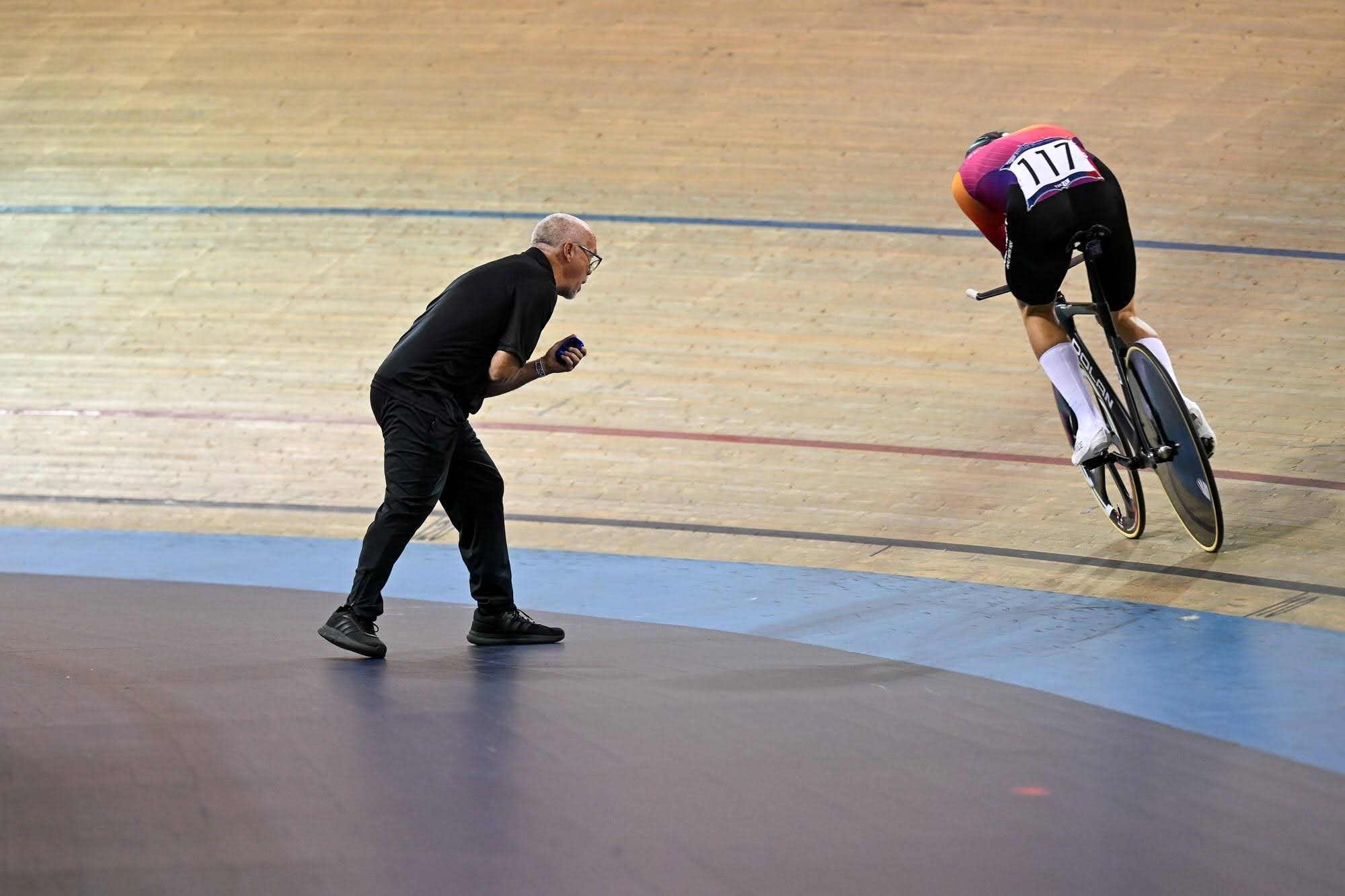 Coach holding a rider in a custom Sportkraft skinsuit at a velodrome standing start