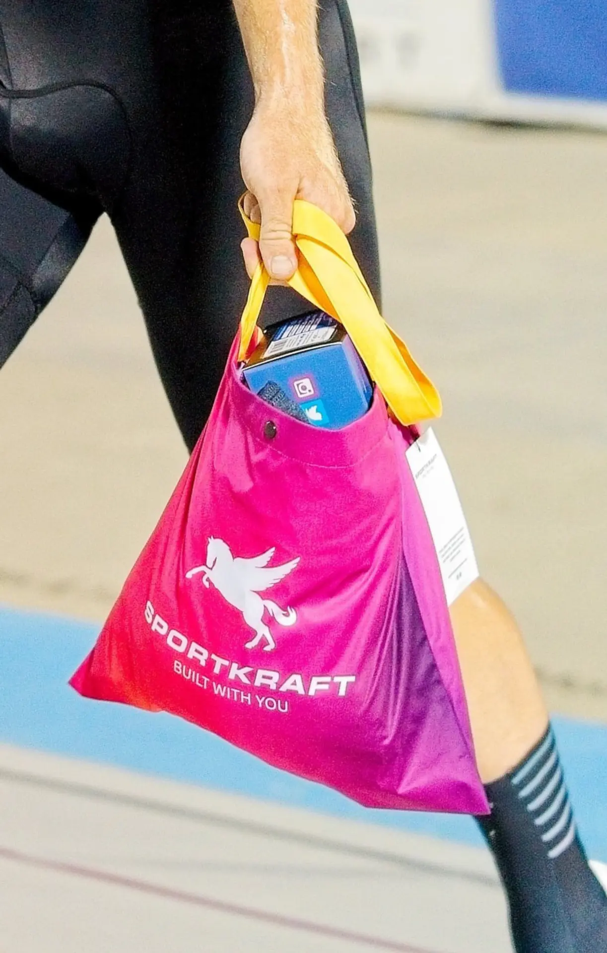 Rider carrying a pink SPORTKRAFT musette with yellow strap and white Pegasus logo