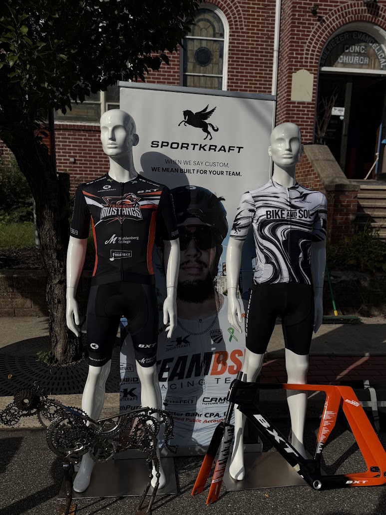 Two custom Sportkraft team kits displayed on mannequins beside a Sportkraft banner at a race expo